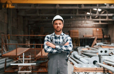 Standing with arms crossed. Factory male worker in uniform is indoors