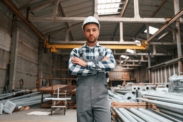 Fototapeta premium Standing with arms crossed. Factory male worker in uniform is indoors
