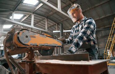 Cutting the wood by saw. Factory male worker in uniform is indoors