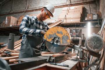 Cutting the wood by saw. Factory male worker in uniform is indoors