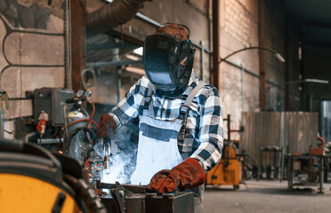In protective mask. Welding the iron. Factory male worker in uniform is indoors