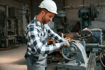 Side view. Using machine. Factory male worker in uniform is indoors