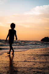 Fototapeta na wymiar silhouette of a child walking by the beach during golden sunset.