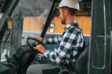 Driving the forklift. Factory male worker in uniform is indoors