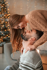 Woman is standing and looking at her man from above. Lovely young couple are celebrating New Year at home