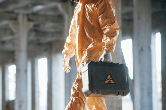 The case with biohazard sign on it. Man dressed in chemical protection suit in the ruins of the post apocalyptic building