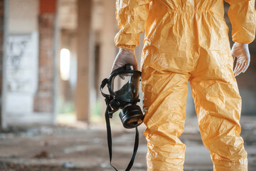 Respirator in hand. Man dressed in chemical protection suit in the ruins of the post apocalyptic...
