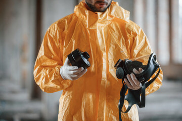 Holding a respirator. Man dressed in chemical protection suit in the ruins of the post apocalyptic...