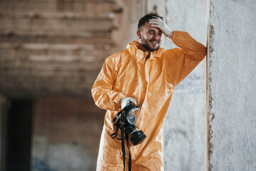 Holding a respirator. Man dressed in chemical protection suit in the ruins of the post apocalyptic...