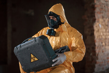 Sitting with radioactive case. Man dressed in chemical protection suit in the ruins of the post apocalyptic building