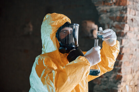 A test tube with radioactive materials. Man dressed in chemical protection suit in the ruins of the post apocalyptic building