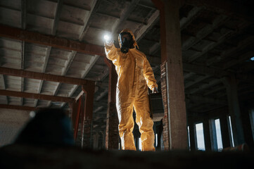 Using the flashlight. Man dressed in chemical protection suit in the ruins of the post apocalyptic building