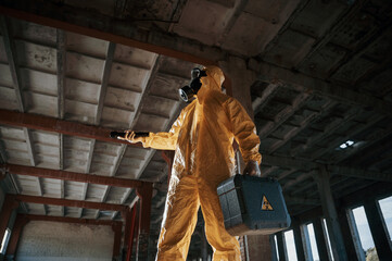 Using the flashlight. Man dressed in chemical protection suit in the ruins of the post apocalyptic building