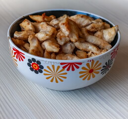 Pieces of fried chicken in a ceramic cup close-up on the background of a light kitchen table
