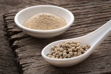 whole white peppercorns on spoon on wood table