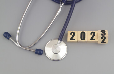 Changes in medicine and health care in year 2023. Stethoscope and numbers 2022 and 2023 on wooden cubes on gray background. 