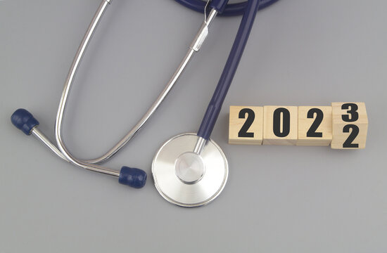 Changes in medicine and health care in year 2023. Stethoscope and numbers 2022 and 2023 on wooden cubes on gray background.