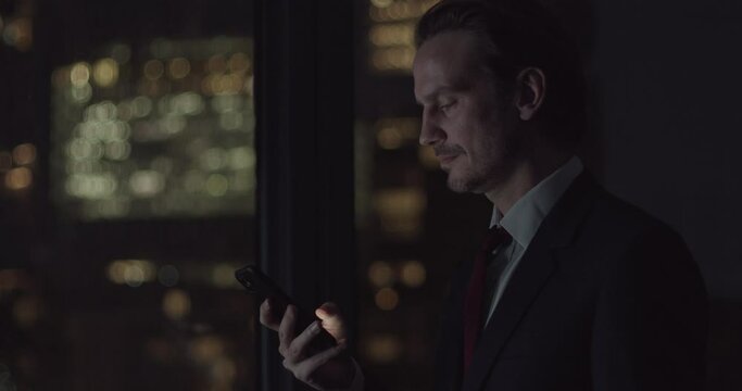 Businessman using Smart phone Working Late in Office with City Skyline