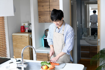 キッチンで料理をするエプロン姿の若い男性