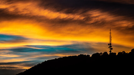 Silhouette of a telecommunication tower on a hill in a sunset with colorful dramatic clouds