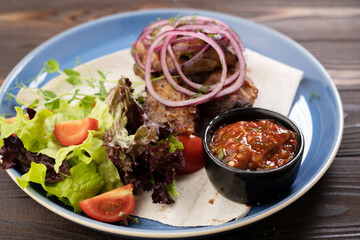 Grilled pork dish with fresh vegetables. food foto of grilled pork cubes with onion and lettuce. Tasty meat with vegetables cooking in restaurant