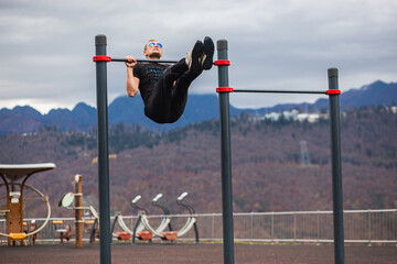 Fototapeta na wymiar Strong man pumps abdominal muscles on uneven bars, rear view. Workout in the cold mountains