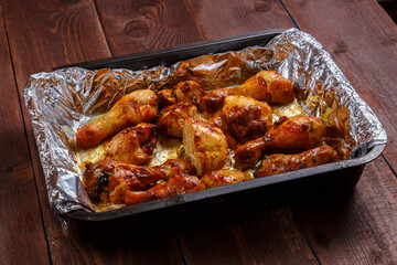 Baked chicken drumsticks in sauce and herbs on foil on a baking sheet.