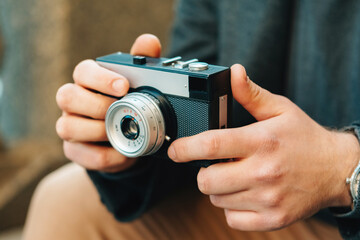 Strong hands of a young man are holding a vintage photo camera in street.