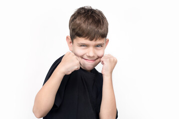 A young boy on a white background holds his fists in front of him and smiles, he has the emotions...