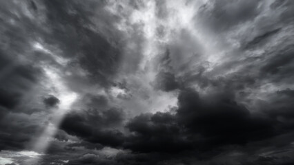 dark dramatic sky with black stormy clouds before rain or snow as abstract background, extreme weather, the sun shines through the clouds, high contrast photo