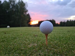 Closeup of golf ball on a tee and sunset or sunrise