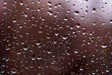 Textured surface of drops of autumn cold rain on window glass against blurred background of an empty dark city park. Rainy weather.