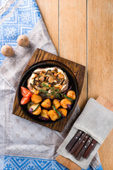 Pork with fried mushrooms, potatoes, zucchini and onions in a cast iron pan.