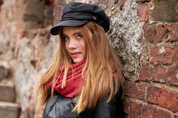Girl in a black cap with a red scarf against a brick wall