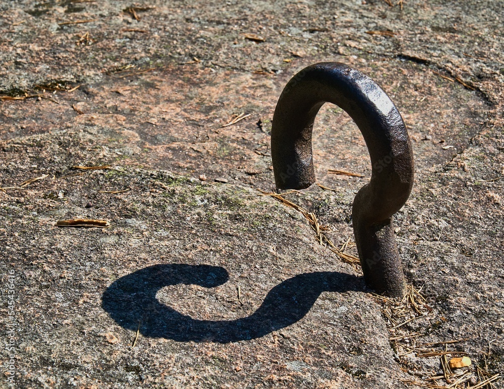 Sticker Closeup shot of an old metal hook with its shadow on the ground in sunny weather