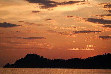 Dramatic scenery of vibrant sunset in the cloudy sky with silhouettes of hills in the background