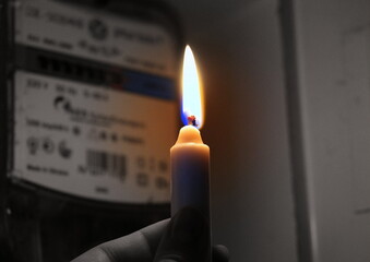Candle in hand shines in the dark near the electricity meter during a power outage at home. City,...