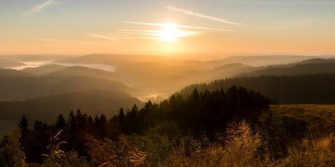 Bright sun in orange sunset sky shining above Black Forest mountain range in Germany