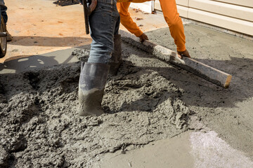 Workers construct new sidewalk adjacent to house by pouring cement on side house as part of...