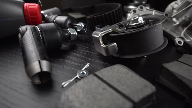 Lot of auto parts lie on wooden black background. Engine and suspension parts, swivel knuckle, joint and engine parts unfolded. New spare parts. Bearings . Play by light. Hanging on table.