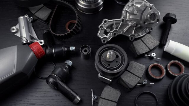 Lot of auto parts lie on wooden black background. Engine and suspension parts, swivel knuckle, joint and engine parts unfolded. New spare parts. Bearings . Play by light. Hanging on table.