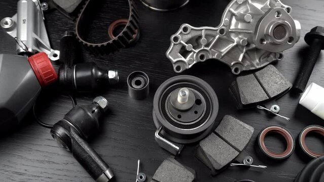 Lot of auto parts lie on wooden black background. Engine and suspension parts, swivel knuckle, joint and engine parts unfolded. New spare parts. Bearings . Play by light. Hanging on table.