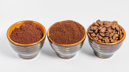 three small saucers with coffee beans, ground coffee and cocoa on a white background.