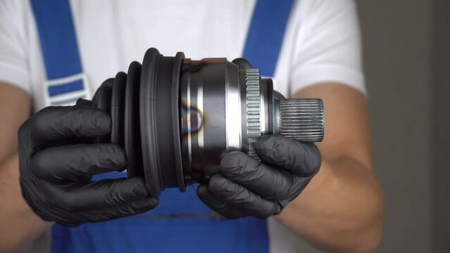 Car mechanic in blue jumpsuit holds in his hands hinge of equal angular velocities of car and puts anther on it.. Spare parts protection concept against dust and dirt. auto parts. shows class sign.