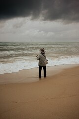 Vertical shot of a fisherman on the beach against the background of the stormy sky and sea.