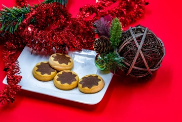Tuinposter Closeup shot of of cookies on a plate alongside Christmas ornaments isolated on a red background © Adrian Vaida/Wirestock Creators