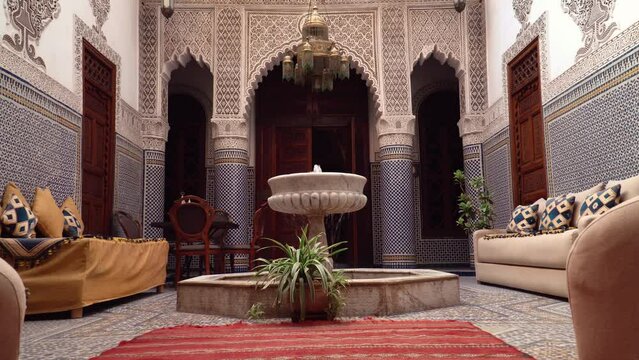 Interior footage of a traditional Moroccan Riad. Courtyard of Riad with fountain, furniture and ornate carvings and tiles.