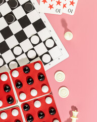 Board games. Various board games with chess pieces, checkers and playing cards on a pink...