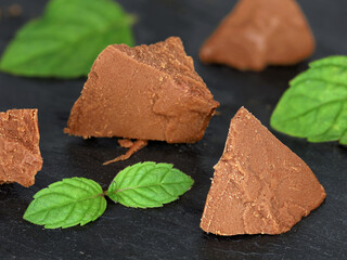 Sweet chocolate hazelnut nougat pieces with mint leaves isolated on black slate board, as baking...