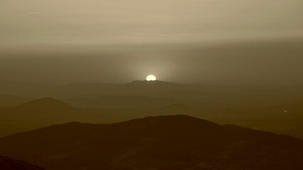Beautiful shot of the sun shining over a hill in a foggy sky
